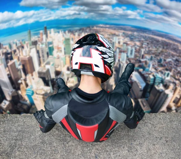 Pengendara sepeda motor dengan perlengkapan lengkap dan helm duduk di gedung tinggi . — Stok Foto