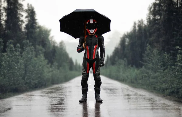 Motorcyclist in full gear and helmet with umbrella in the rain.
