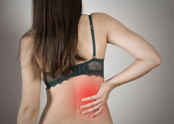 Low back pain in a woman. Highlighted in red. On a gray background. Close up.