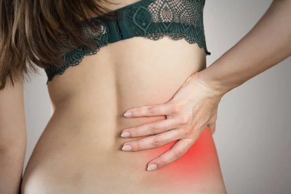 Low back pain in a woman. Highlighted in red. On a gray background. Close up.