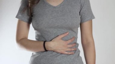 Kızda karın ağrısı var. Kapatın. Gri bir arkaplanda izole edilmiş.