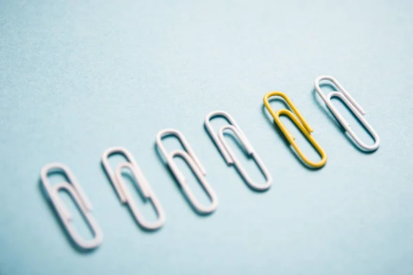 Yellow paper clip amongst white clips symbolises the concept of standing out from the crowd.