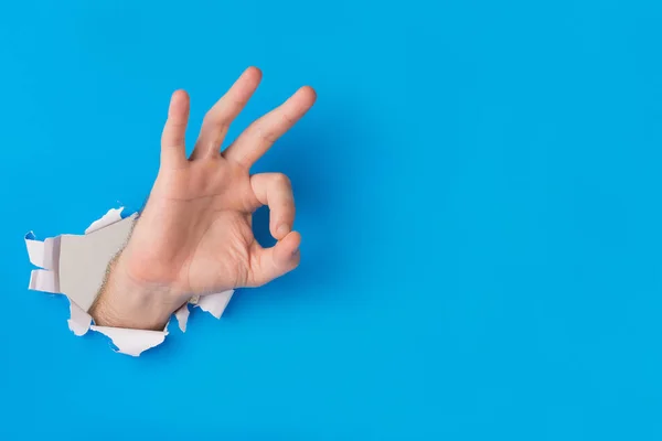 Masculino mão rasgando através de azul papel fundo criação ok gest — Fotografia de Stock