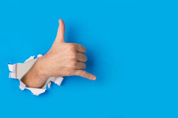 Mão masculina rasgando através de fundo de papel azul criando um shaka — Fotografia de Stock