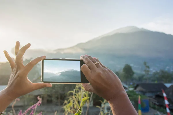 Womans hand taking photo of mouintain in late afternoon with pho