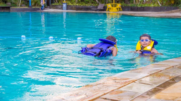 Young boy and girl happily swimming in pool with life jacket on. Childhood lifestyle and water safety concept image.