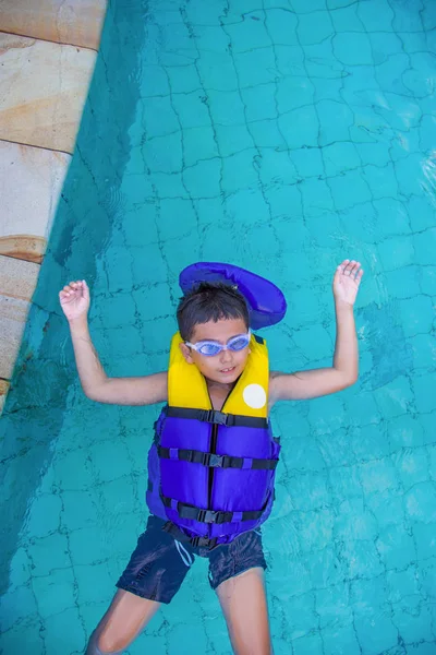 Boy swimming with life vest and googles on shot from above - childhood lifestyle and water safety concept image