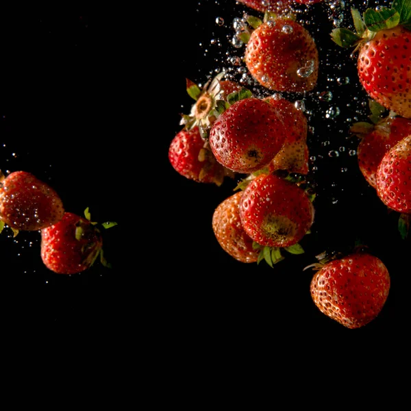 Ripe organic strawberries falling into water with bubbles and dark black background. Healthy food concept image — Stock Photo, Image