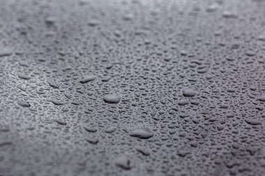 Siyah metal bir yüzeye bir damla su. Merkezde seçmeli odak.