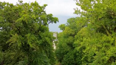 Etrafı yemyeşil ağaçlar ve su kanallarıyla çevrili tarihi bir şatonun havadan görünüşü. Bina zarif mimarisiyle göze çarpıyor, huzurlu kırsal alana karışıyor..
