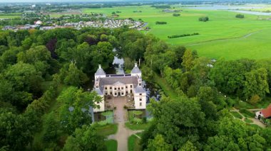 Etrafı yemyeşil ağaçlar ve su kanallarıyla çevrili tarihi bir şatonun havadan görünüşü. Bina zarif mimarisiyle göze çarpıyor, huzurlu kırsal alana karışıyor..