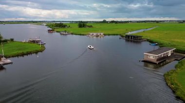Huzurlu bir nehir manzarası. Yeşil tarlalardan, geleneksel evlerden ve kırsal kesimin cazibesini yakalayan tarihi yel değirmeninden sakin bir şekilde geçen tekneler..