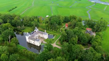Etrafı yemyeşil ağaçlar ve su kanallarıyla çevrili tarihi bir şatonun havadan görünüşü. Bina zarif mimarisiyle göze çarpıyor, huzurlu kırsal alana karışıyor..