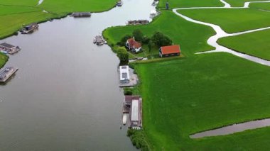 Bereketli yeşil tarlalar ve dolambaçlı kanallarla çevrili nehir kenarındaki evler ve teknelerin manzarası huzurlu bir kırsal alanı yakalıyor..