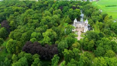 Etrafı yemyeşil ağaçlar ve su kanallarıyla çevrili tarihi bir şatonun havadan görünüşü. Bina zarif mimarisiyle göze çarpıyor, huzurlu kırsal alana karışıyor..