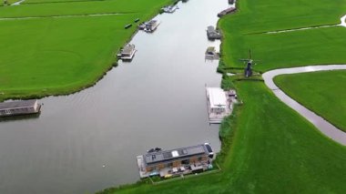 Huzurlu bir nehir manzarası. Yeşil tarlalardan, geleneksel evlerden ve kırsal kesimin cazibesini yakalayan tarihi yel değirmeninden sakin bir şekilde geçen tekneler..