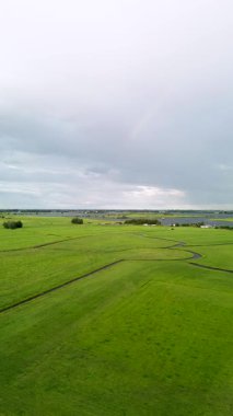 Bereketli yeşil tarlaların hava görüntüsü kıvrımlı su yollarıyla bölünmüş, bulutlu bir gökyüzünün altında nehir ve uzak ufuk, barışçıl bir kırsal alan yaratıyor..