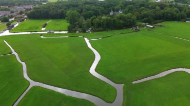 Dolambaçlı bir dere geniş yeşil çayırlar boyunca akar, orman kenarındaki küçük kırsal ahırlar ve sakin, bulutlu bir gökyüzü altında uzak bir kasaba.