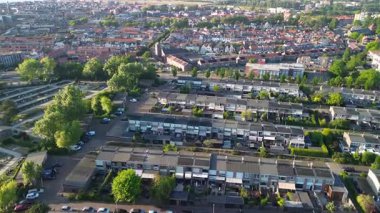 Modern evler, yeşil bahçeler ve ağaçlarla kaplı caddelerle dolu bir banliyö manzarası. Arka planda kırmızı çatıları olan yoğun bir kasaba ve bir mezarlık görülebilir.