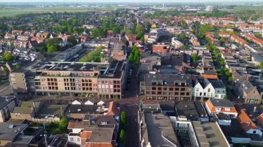 Modern ve geleneksel binalar, dar sokaklar ve açık araziler ve açık gökyüzü altındaki uzak manzaralarla çevrili yeşil ağaçlarla dolu bir Avrupa kasabasının havadan görünüşü..