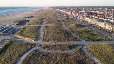 Kum tepeleri, yürüyüş yolları ve kıyı şeridi boyunca uzanan geniş bir sahil manzarası. Sahil şeridinde sıra sıra evler ve binalar var..