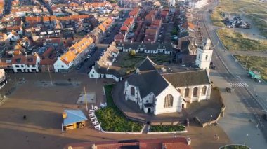 Tarihi beyaz bir kilisesi, kırmızı çatılı evleri ve yakındaki kum tepeleri olan bir sahil kasabasının havadan görünüşü geleneksel mimariyi akşam ışığı altında deniz manzarasıyla harmanlıyor..