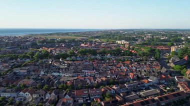 Turuncu çatıları, yoğun evleri ve yeşillikleri olan temiz mavi gökyüzü altında denize ve kırsala doğru uzanan Avrupa kıyı kasabasının havadan görünüşü.