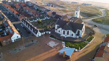 Tarihi beyaz bir kilisesi, kırmızı çatılı evleri ve yakındaki kum tepeleri olan bir sahil kasabasının havadan görünüşü geleneksel mimariyi akşam ışığı altında deniz manzarasıyla harmanlıyor..