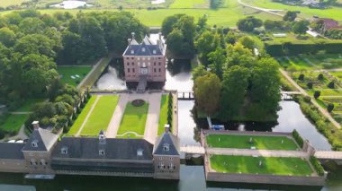 Su ve yeşilliklerle çevrili büyük bir arazinin havadan görünüşü. Tuğla binalar, köprüler ve manikürlü çimenler tarih ve zarafetle dolu simetrik, şatovari bir manzara yaratır..