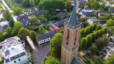 Kırmızı kiremitli çatıları, yemyeşil otlağı ve merkezinde uzun bir kilise kulesi olan büyüleyici bir Avrupa kasabasının havadan görünüşü. Dar sokaklar ve rahat evler huzurlu, resimli bir manzara yaratır..