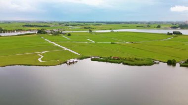 Geniş bir göl, yeşil alanlar ve dar kanallarla huzurlu bir kırsal alan manzarası. Suyun yakınındaki dağınık evler bu güzel, sakin kırsal bölgeye cazibe katıyor..