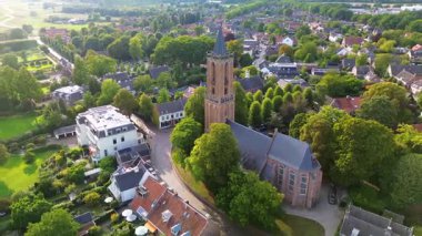 Kırmızı kiremitli çatıları, yemyeşil otlağı ve merkezinde uzun bir kilise kulesi olan büyüleyici bir Avrupa kasabasının havadan görünüşü. Dar sokaklar ve rahat evler huzurlu, resimli bir manzara yaratır..