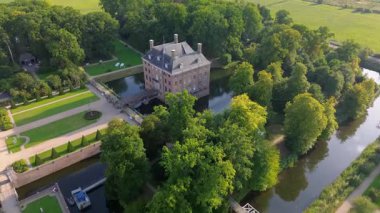 Hendek, bahçeler ve ağaçlarla çevrili, kiremitli çatılı tarihi bir tuğla kalenin hava manzarası. Kırsal kesim, mimarinin zarafetini ve bereketli manzarayı ön plana çıkarıyor..