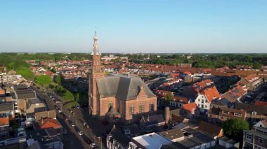 Merkezi kırmızı tuğlalı kilise ve çan kulesine sahip, turuncu çatıları, dar sokakları ve açık mavi gökyüzü altında yemyeşil yemyeşil evlerle çevrili bir Avrupa kasabası..