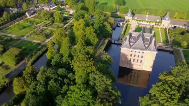 Hendek, bahçeler ve ağaçlarla çevrili, kiremitli çatılı tarihi bir tuğla kalenin hava manzarası. Kırsal kesim, mimarinin zarafetini ve bereketli manzarayı ön plana çıkarıyor..