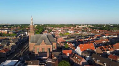 Merkezi kırmızı tuğlalı kilise ve çan kulesine sahip, turuncu çatıları, dar sokakları ve açık mavi gökyüzü altında yemyeşil yemyeşil evlerle çevrili bir Avrupa kasabası..