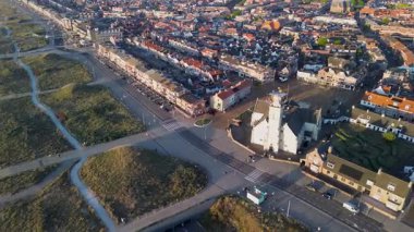 Beyaz bir kilisesi, sahil kumulları ve yürüyüş yolları olan bir sahil kasabasının havadan görünüşü. Binalar, sokaklar ve doğal elementlerin karışımı organize deniz kenarı kentsel planlamasını yansıtıyor.