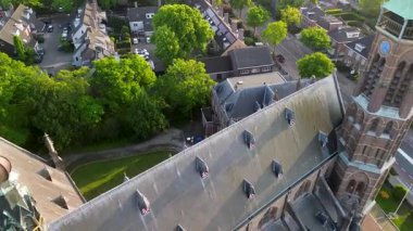 Gotik Diriliş Kilisesi 'nin havadan görünüşü. Uzun saat kulesi, süslü taş işçiliği ve kızıl aksanlı yatakhaneleri var. Şehir binaları ve ağaçlarla çevrili bu sahne, tarihi şehir hayatıyla harmanlıyor..