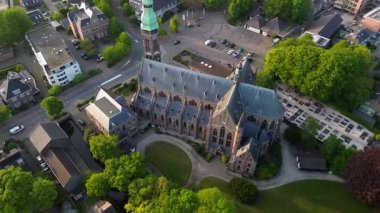 Ağaçlar, yollar ve karışık kullanım alanları olan yeşil kulesi olan Gotik tarzı bir kilisenin havadan görünüşü. Taş mimarisi bu iyi korunmuş şehir manzarasında göze çarpıyor..