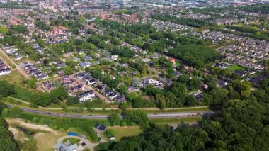 Ayrılmış evleri, ağaçlarla kaplı caddeleri ve büyük bir yolu olan bir banliyö mahallesinin havadan görüntüsü. Ormanlık alan ve dairesel garaj yolu olan büyük bir arazi planlanan plana zıtlık ekler.