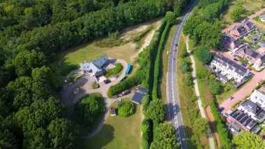 Ormanlık arazisi, dairesel garaj yolu ve banliyö mahallesi olan yarı kırsal bir bölgenin havadan görünüşü. Olay yeri, organize konut geliştirme ile tenha yaşam ile çelişiyor.