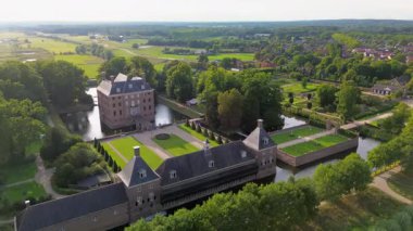 Hendek, bahçeler ve ağaçlarla çevrili, kiremitli çatılı tarihi bir tuğla kalenin hava manzarası. Kırsal kesim, mimarinin zarafetini ve bereketli manzarayı ön plana çıkarıyor..