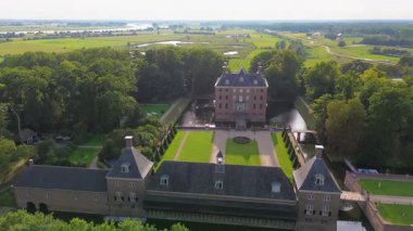 Hendek, bahçeler ve ağaçlarla çevrili, kiremitli çatılı tarihi bir tuğla kalenin hava manzarası. Kırsal kesim, mimarinin zarafetini ve bereketli manzarayı ön plana çıkarıyor..