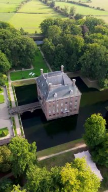 Hendek, bahçeler ve ağaçlarla çevrili, kiremitli çatılı tarihi bir tuğla kalenin hava manzarası. Kırsal kesim, mimarinin zarafetini ve bereketli manzarayı ön plana çıkarıyor..