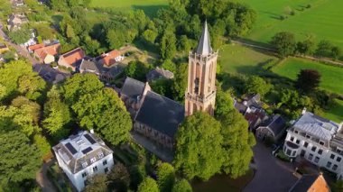Kırmızı kiremitli çatıları, yemyeşil otlağı ve merkezinde uzun bir kilise kulesi olan büyüleyici bir Avrupa kasabasının havadan görünüşü. Dar sokaklar ve rahat evler huzurlu, resimli bir manzara yaratır..