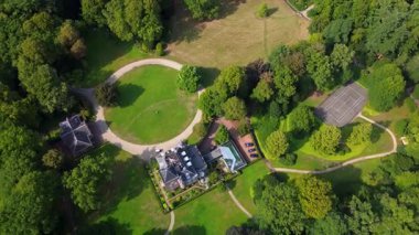 Geniş bir köşkü, manzarası geniş bir arazisi, dolambaçlı yolları ve yemyeşil ağaçları ve açık otlaklarla çevrili bir tenis sahası olan büyük bir arazinin havadan görünüşü..