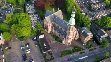 Ağaçlar, yollar ve daha küçük yapılarla çevrili yüksek kulesi olan tarihi yeşil çatılı bir binanın havadan görünüşü Gothicstyle mimarisini düzenli bir kentsel manzara ile harmanlıyor..