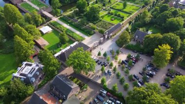 Hendek, bahçeler ve ağaçlarla çevrili, kiremitli çatılı tarihi bir tuğla kalenin hava manzarası. Kırsal kesim, mimarinin zarafetini ve bereketli manzarayı ön plana çıkarıyor..