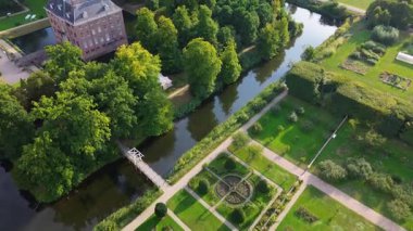 Hendek, bahçeler ve ağaçlarla çevrili, kiremitli çatılı tarihi bir tuğla kalenin hava manzarası. Kırsal kesim, mimarinin zarafetini ve bereketli manzarayı ön plana çıkarıyor..