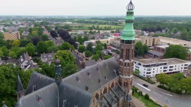Ağaçlar, yollar ve karışık kullanım binalarıyla çevrili yeşil kulesi olan Gotik bir kilisenin havadan görünüşü. Taş mimarisi bu iyi korunmuş kentsel alanda göze çarpıyor..